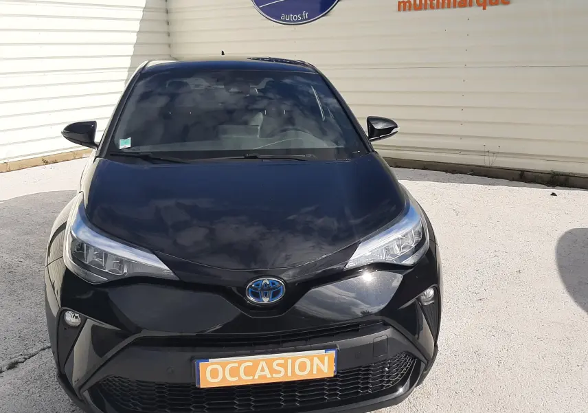 Vue avant d'un Toyota C-HR 1.8 Hybrid 122 Design noir brillant, avec calandre distinctive et phares LED allumés.