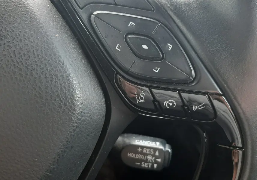 Gros plan sur les commandes noires au volant côté gauche du Toyota C-HR 1.8 Hybrid 2023, avec boutons multifonctions.