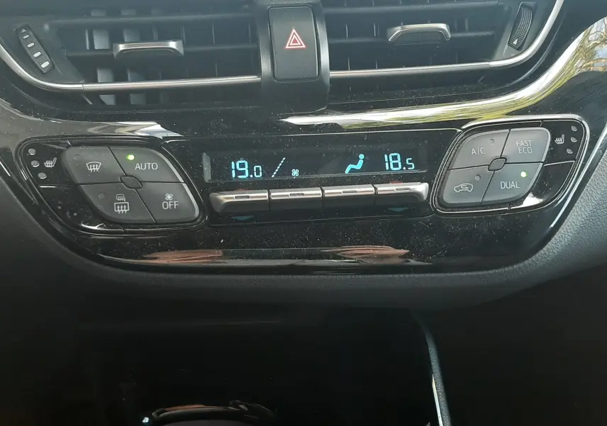 Vue rapprochée du tableau de bord noir du Toyota C-HR 1.8 Hybrid 2023, affichant la climatisation automatique dual zone.
