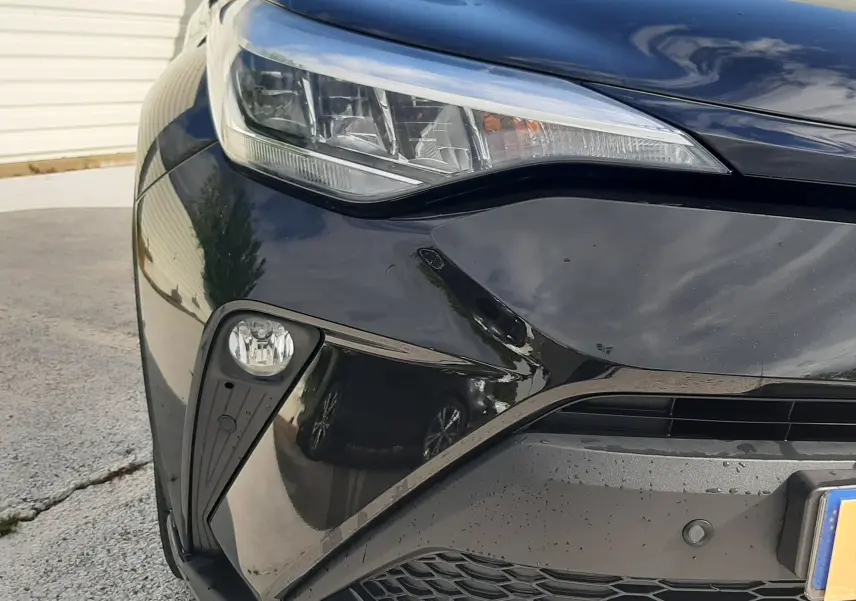Gros plan sur l'avant gauche du Toyota C-HR 1.8 Hybrid noir 2023, mettant en valeur le phare et la calandre hexagonale.