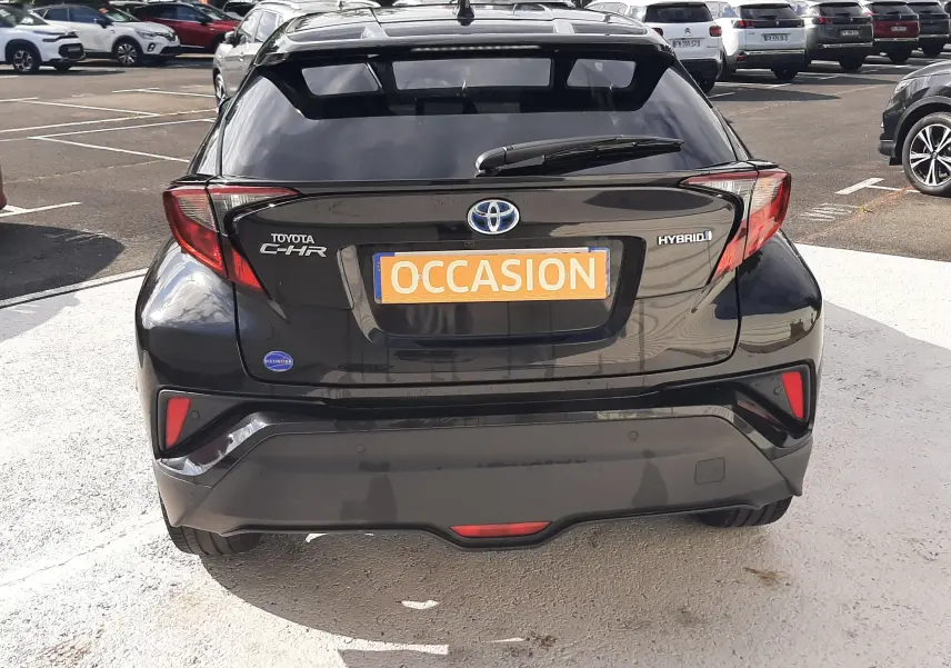 Vue arrière d'un Toyota C-HR noir hybride 2023 avec badge "HYBRID" et plaque "OCCASION" visible sur un parking.