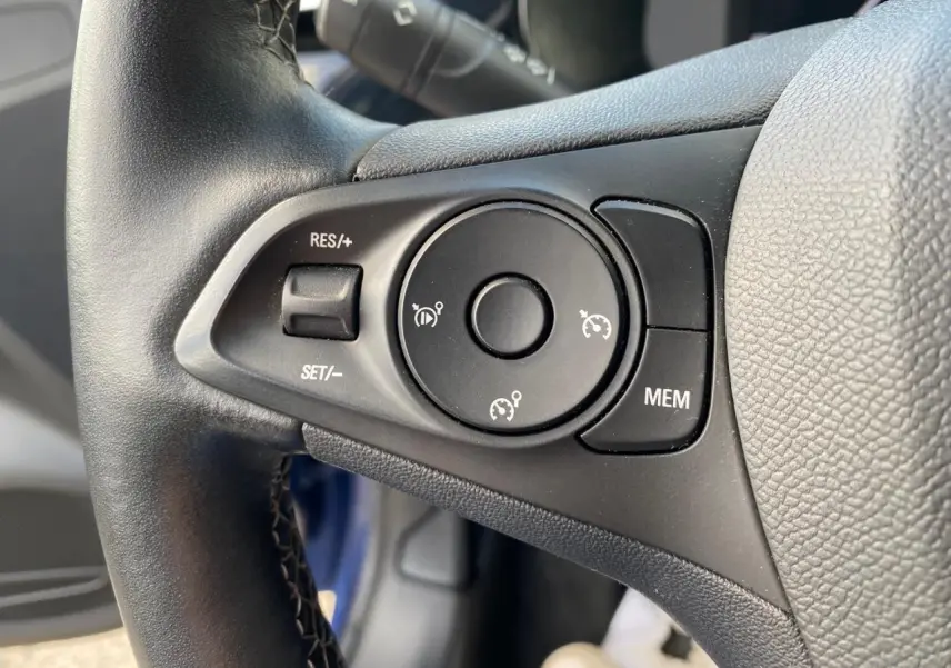 Gros plan sur les commandes du régulateur de vitesse au volant en cuir d'une Opel Corsa bleu nautique 2021.