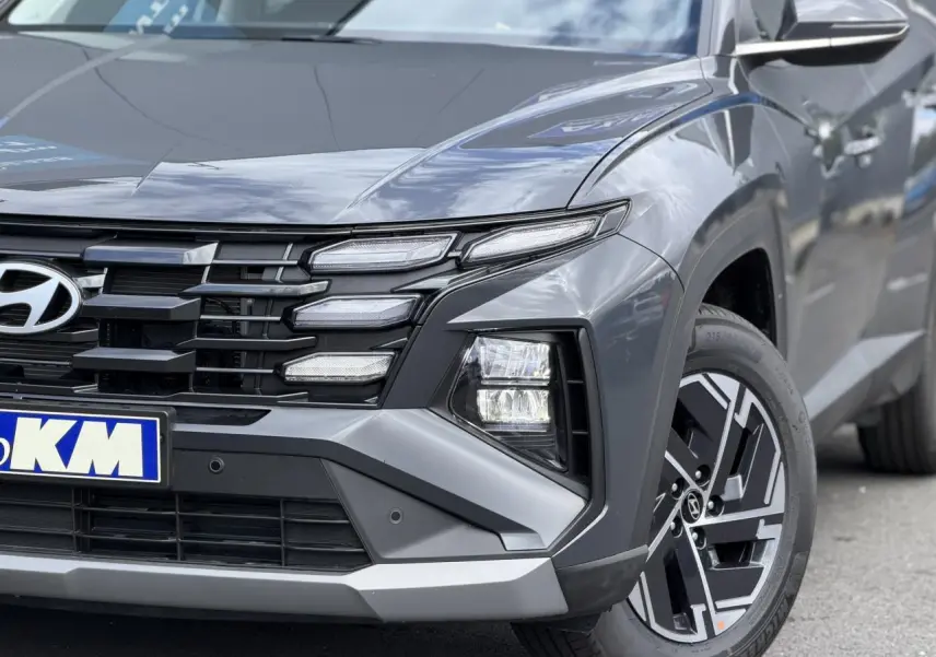 Vue avant droite du Hyundai Tucson 2026 Ecotronic Gray, mettant en valeur la calandre noire et les phares LED distinctifs.
