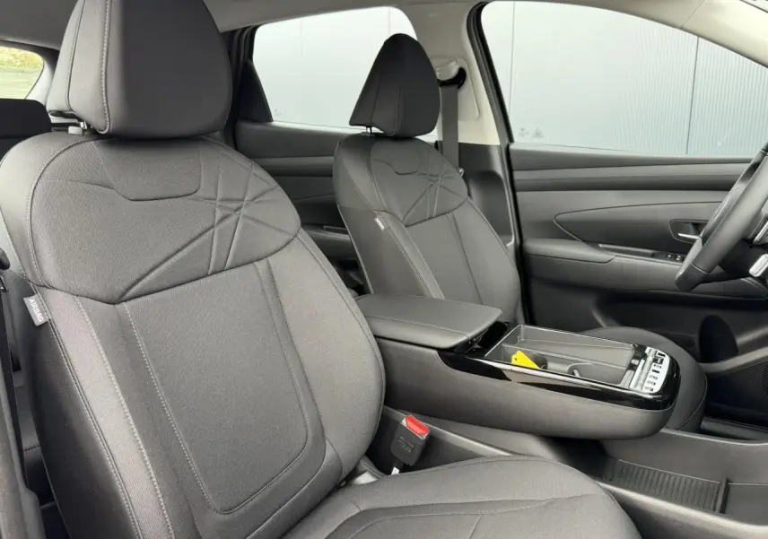 Vue intérieure du Hyundai Tucson 2026, sièges avant en tissu gris foncé avec accoudoir central et console moderne.