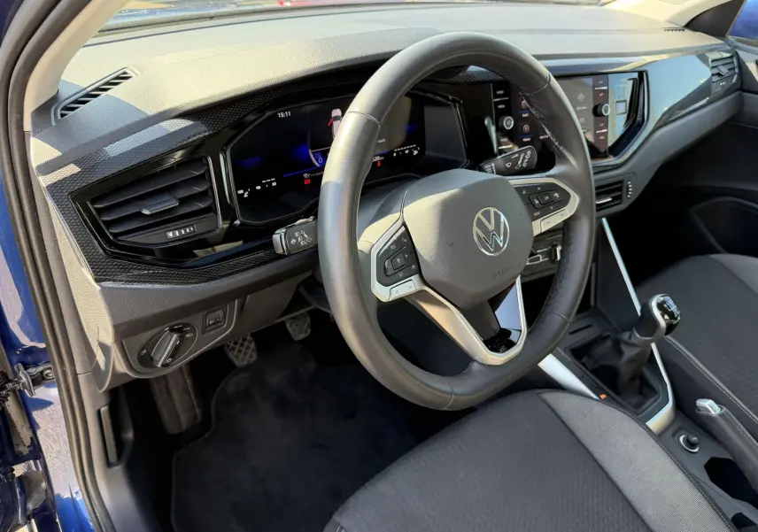 Vue intérieure côté conducteur du Volkswagen Taigo bleu, volant cuir multifonction et levier de vitesse manuel visible.