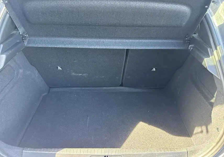Coffre ouvert de la Peugeot 208 1.2 100 allure gris artense, montrant l'espace de chargement vide et les dossiers de banquette rabattables.