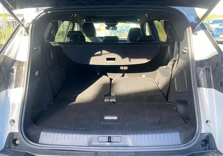 Coffre ouvert vu de l'arrière d'un Peugeot 5008 blanc avec banquette arrière rabattue et cache-bagages déployé.