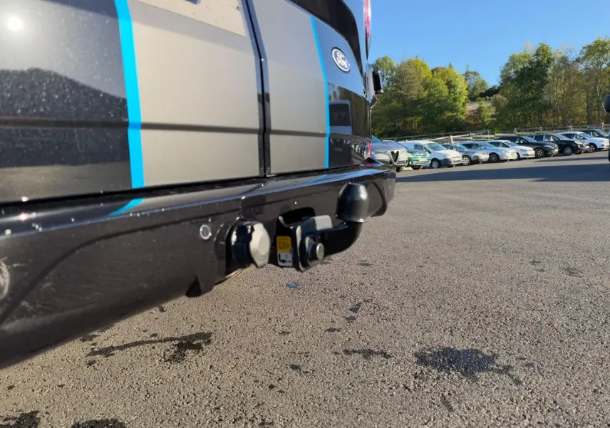 Gros plan sur le crochet d'attelage arrière du Ford Transit Fourgon noir avec bandes bleues, sous un ciel dégagé.