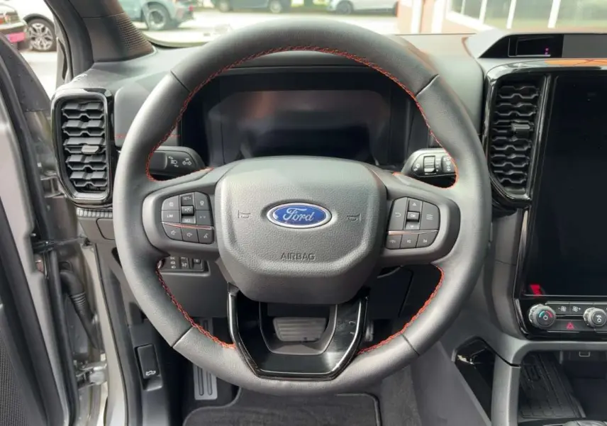 Vue rapprochée du volant cuir noir avec surpiqûres rouges du Ford Ranger Wildtrak Plus 2026 gris iconic, tableau de bord moderne.