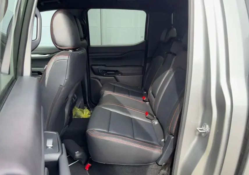 Vue latérale droite sur l'intérieur arrière du Ford Ranger Wildtrak gris iconic avec sièges cuir noirs et surpiqûres orange.