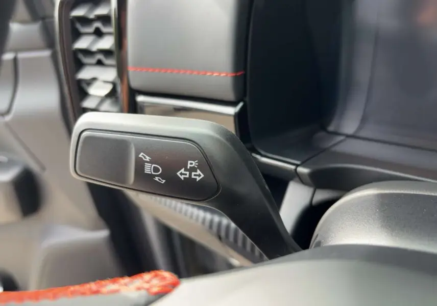 Gros plan sur la commande de clignotant et feux du Ford Ranger Wildtrak Plus 2026, intérieur noir avec surpiqûres rouges.