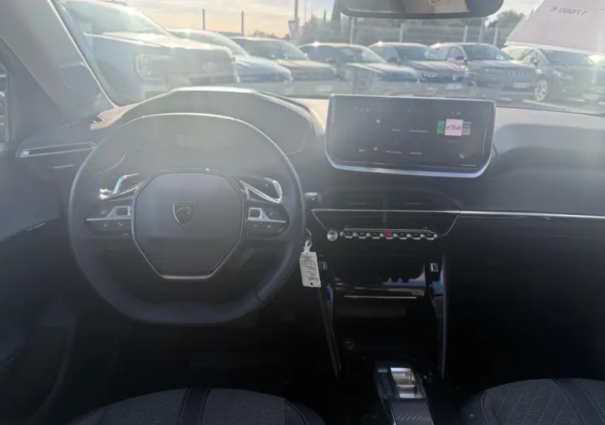 Vue intérieure de face du poste de conduite de la Peugeot 208 Hybrid 110 e-DCS6 Allure 2024 avec écran tactile et volant compact noir.