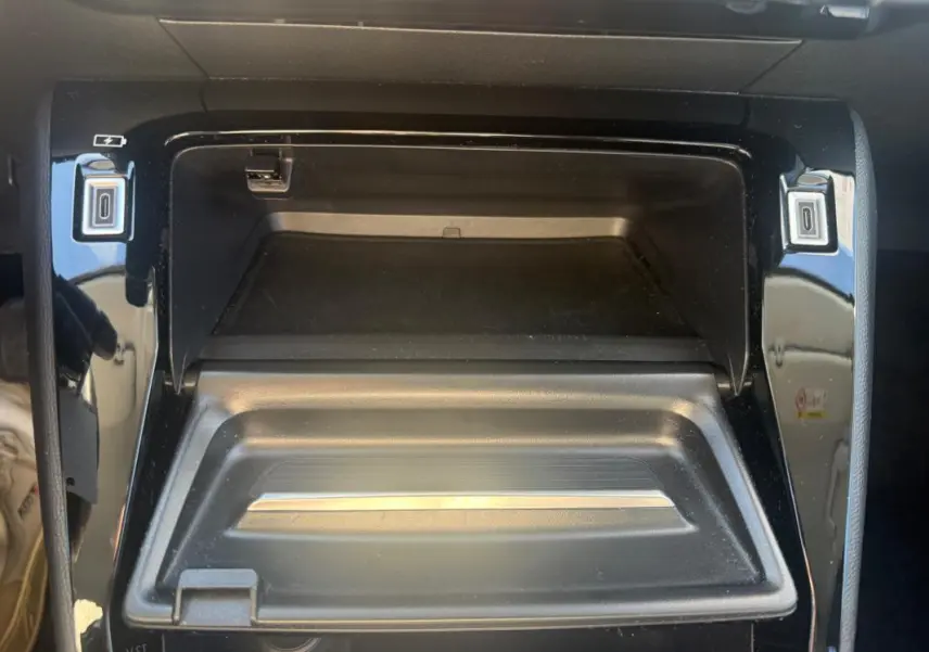 Vue rapprochée de la console centrale noire du Peugeot 208 Hybrid 110 e-DCS6 Allure 2024 avec compartiment ouvert.