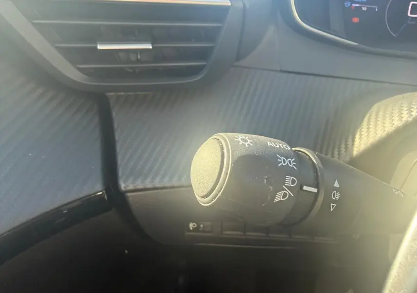 Gros plan sur la commande des phares à gauche du volant dans l’habitacle de la Peugeot 208 Hybrid 110 e-DCS6 Allure 2024.