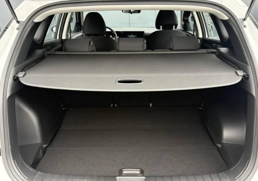 Vue arrière du coffre ouvert du Hyundai Tucson blanc Serenity, avec cache-bagages déployé et intérieur noir.