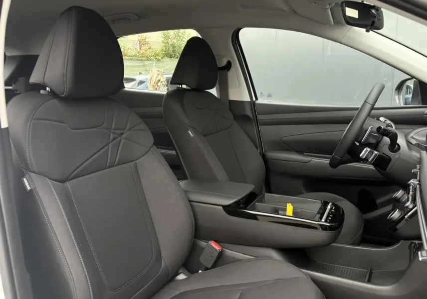 Vue intérieure côté gauche du Hyundai Tucson 2026 avec sièges avant noirs et console centrale moderne.