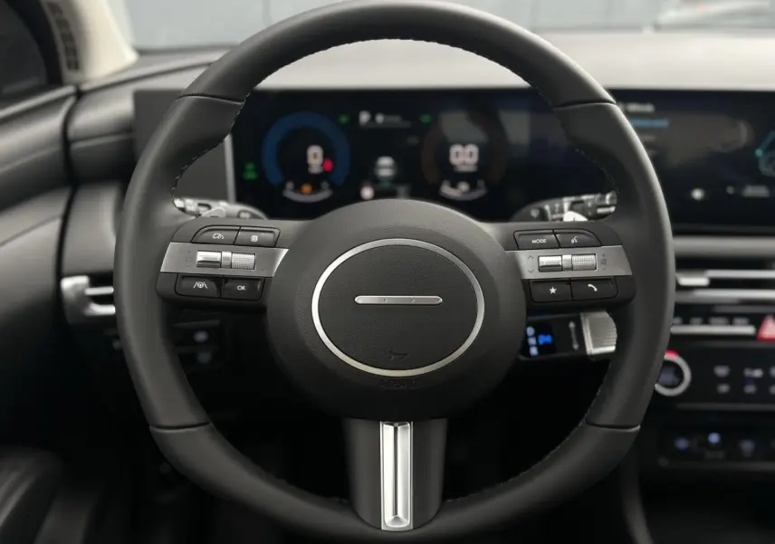 Gros plan sur le volant noir multifonction du Hyundai Tucson 2026 avec tableau de bord numérique en arrière-plan flou.