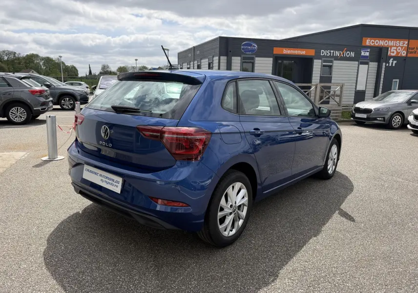 Volkswagen Polo bleue vue en 3/4 arrière droit sur parking, avec jantes alliage et feux arrière LED.