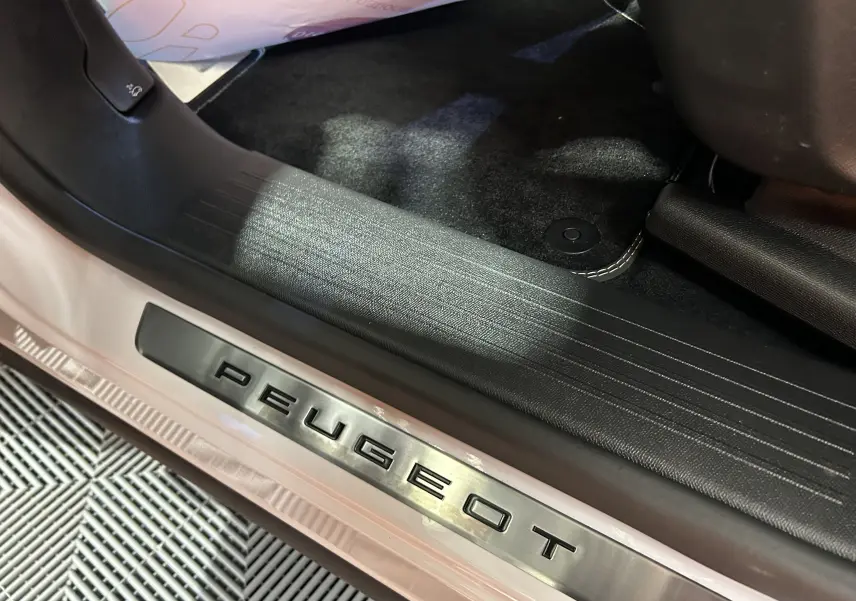 Gros plan sur la plaque de seuil de porte Peugeot en métal brossé, intérieur noir et tapis foncé visibles.