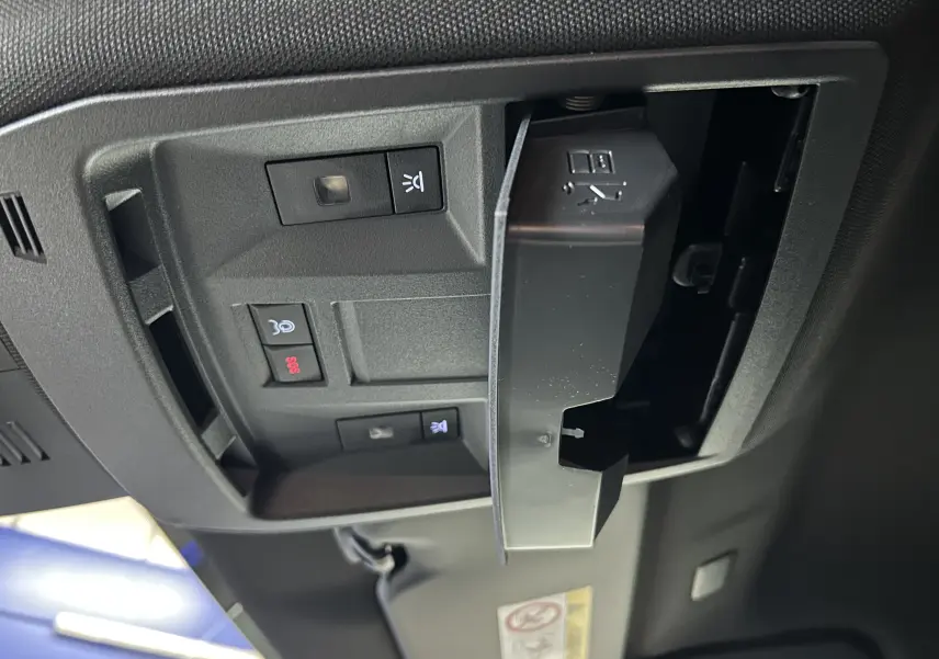 Gros plan sur la console de toit noire avec boutons de commande et compartiment ouvert dans un Peugeot 3008 blanc Okenite.