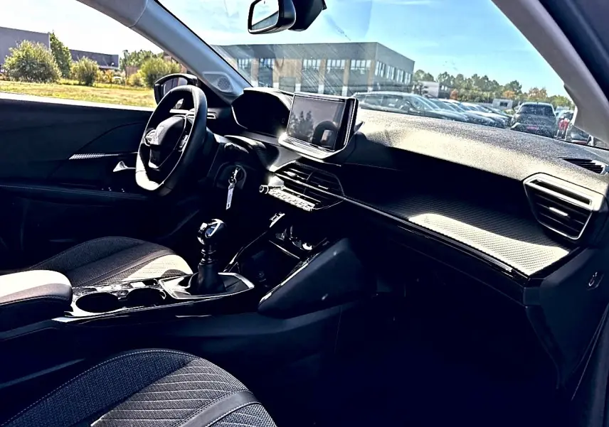 Intérieur de la Peugeot 208 1.2 100 Allure, vue côté conducteur, tableau de bord moderne avec écran tactile et volant noir.