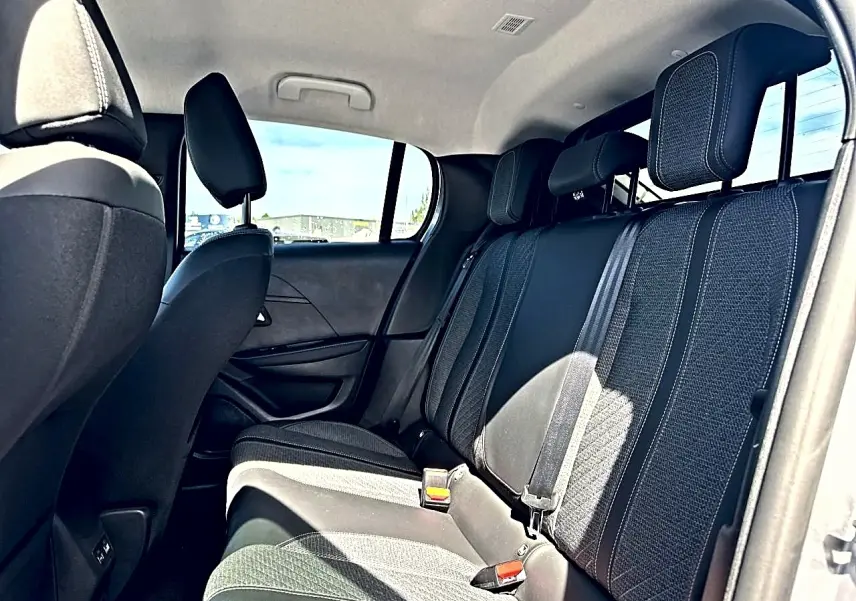 Vue intérieure arrière de la Peugeot 208 1.2 100 Allure avec sièges tissu gris et ceintures de sécurité visibles.