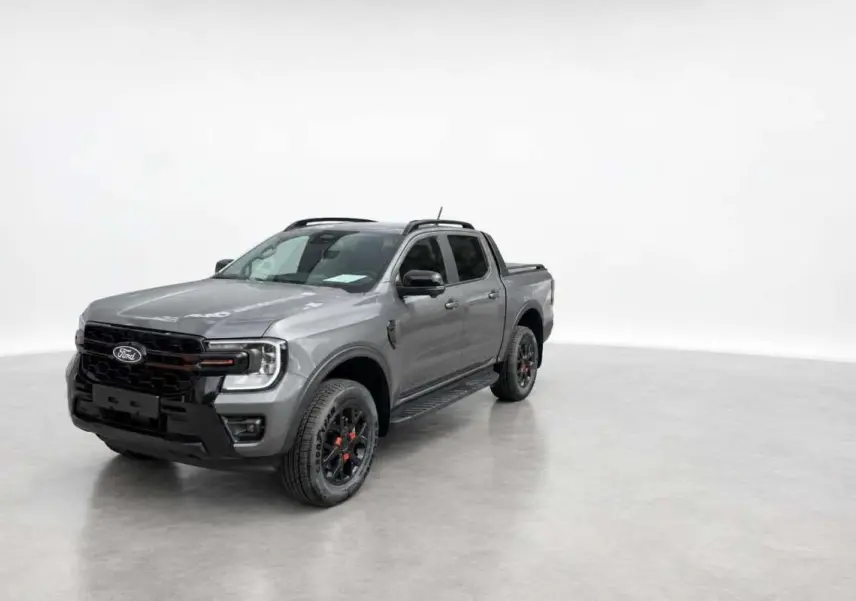 Ford Ranger Wildtrak gris carbone en 3/4 avant droit, avec jantes noires et barres de toit visibles.