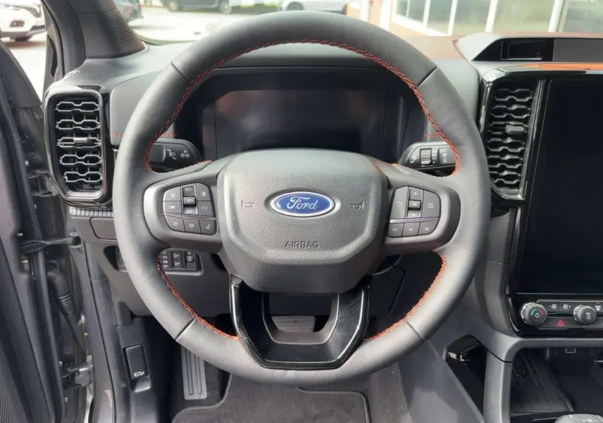 Vue rapprochée du volant cuir noir avec surpiqûres orange du Ford Ranger Wildtrak Plus 2026, tableau de bord partiel visible.