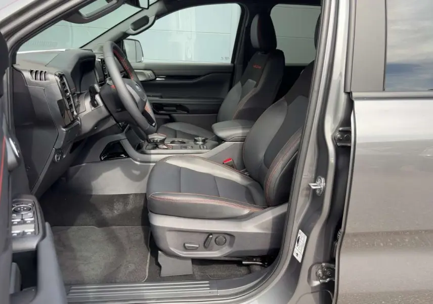 Vue intérieure côté conducteur du Ford Ranger gris carbone 2026, sièges noirs avec surpiqûres rouges et tableau de bord moderne.