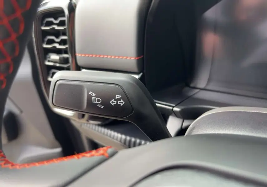 Gros plan sur la manette de clignotant noire avec pictogrammes blancs, volant noir avec surpiqûres rouges dans un Ford Ranger gris carbone.