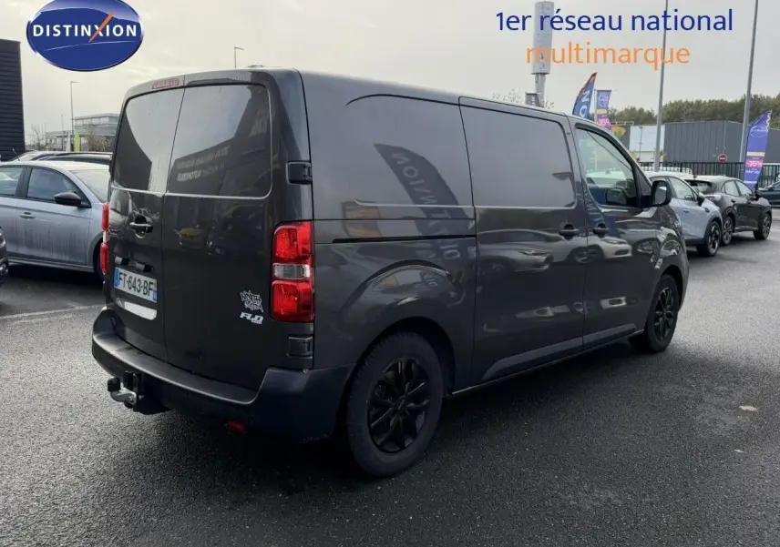 Vue 3/4 arrière droit d'un Opel Vivaro Fourgon gris Pierre de Lune métallisé avec attelage et jantes noires.