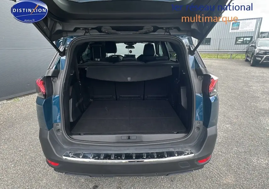 Coffre ouvert d'un Peugeot 5008 bleu vu de l'arrière, montrant l'espace de chargement et la banquette arrière.