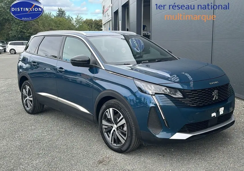 Peugeot 5008 bleu en 3/4 avant droit, avec calandre à damiers chromés et jantes alliage 18 pouces visibles.