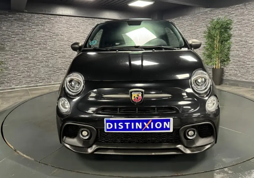 Vue avant d'une ABARTH 595 Competizione noire métallisée avec logo Abarth et phares ronds LED dans un showroom.
