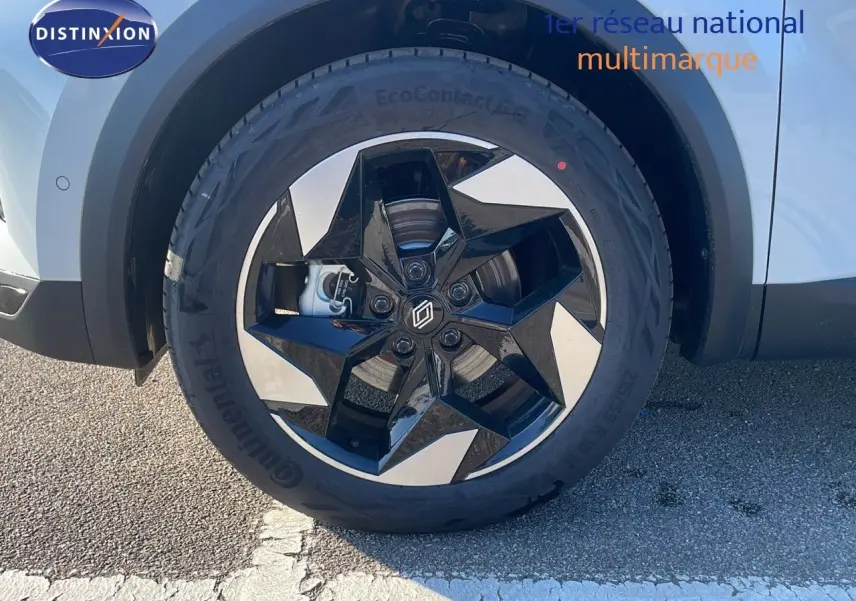 Gros plan sur la roue avant gauche du Renault Captur blanc nacré avec jante noire et argentée au design étoilé.