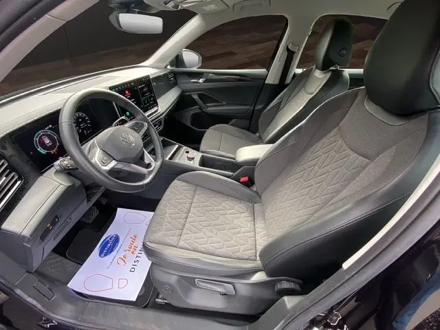 Vue intérieure côté conducteur du Volkswagen Tiguan 2024 avec sièges tissu gris et tableau de bord numérique.