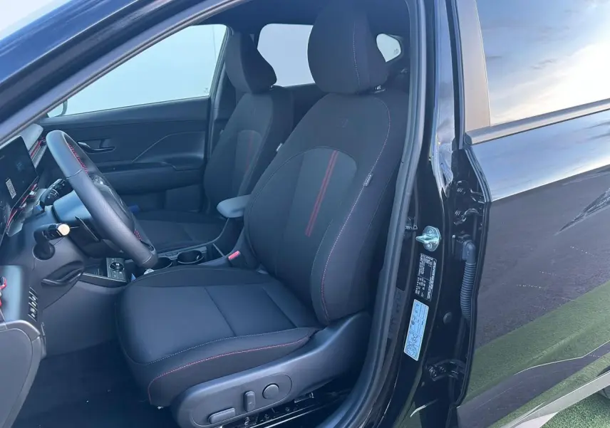 Vue intérieure côté conducteur du Hyundai KONA II noir Abyss Metal, sièges N Line avec surpiqûres rouges et volant cuir.