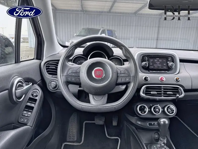 Vue intérieure du tableau de bord et volant cuir multifonction de la Fiat 500X noir Cinéma pastel extra-série, avec écran tactile central.