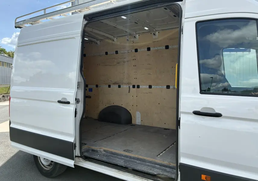 Vue latérale droite d’un Volkswagen Crafter blanc avec porte coulissante ouverte montrant l’intérieur utilitaire en bois.