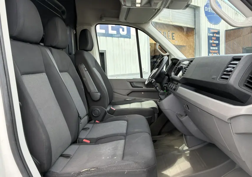 Vue intérieure côté conducteur du Volkswagen Crafter blanc, montrant les sièges avant et le tableau de bord gris.