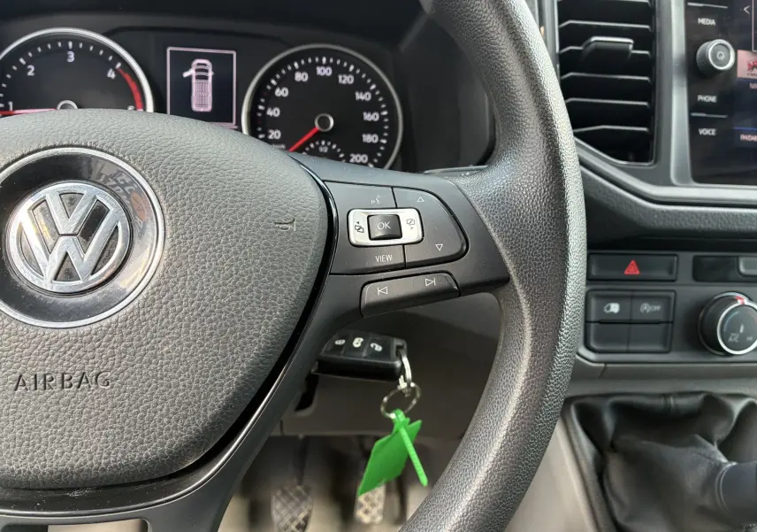 Gros plan sur le volant multifonctions noir et le tableau de bord du Volkswagen Crafter blanc, avec clés et commandes visibles.