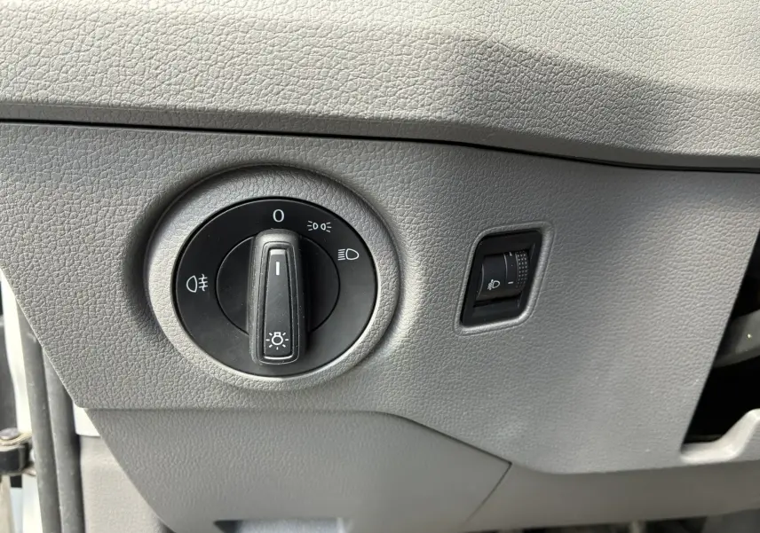 Gros plan sur le bouton de commande des phares et le réglage d’intensité lumineuse dans un Volkswagen Crafter blanc.