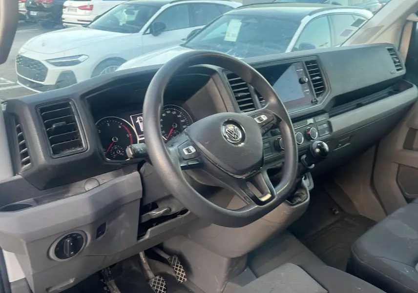 Vue de profil côté droit d'un Volkswagen Crafter blanc avec galerie de toit et double portes arrière ouvertes à 270° visibles en arrière-plan.