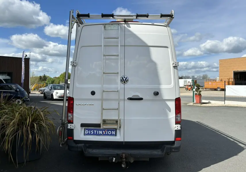 Vue arrière d’un Volkswagen Crafter blanc avec échelle métallique fixée et attelage de remorque visible.