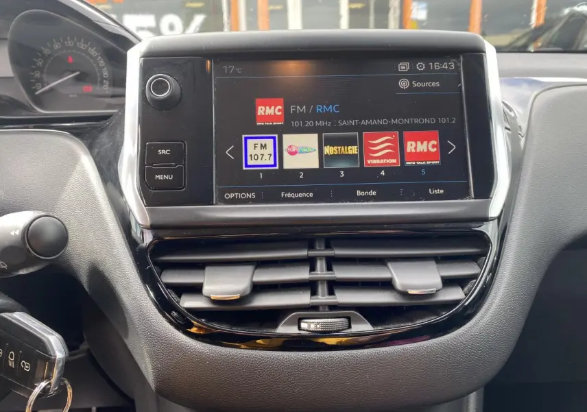Vue rapprochée de l’écran tactile central et tableau de bord de la Peugeot 208 gris, avec affichage radio FM et commandes autour.