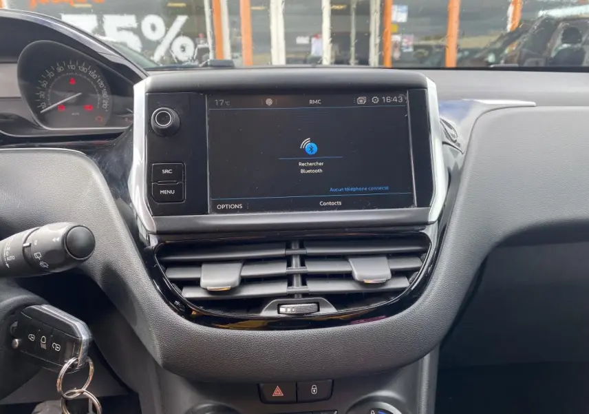 Vue rapprochée du tableau de bord de la Peugeot 208 gris, avec écran tactile central affichant la recherche Bluetooth.