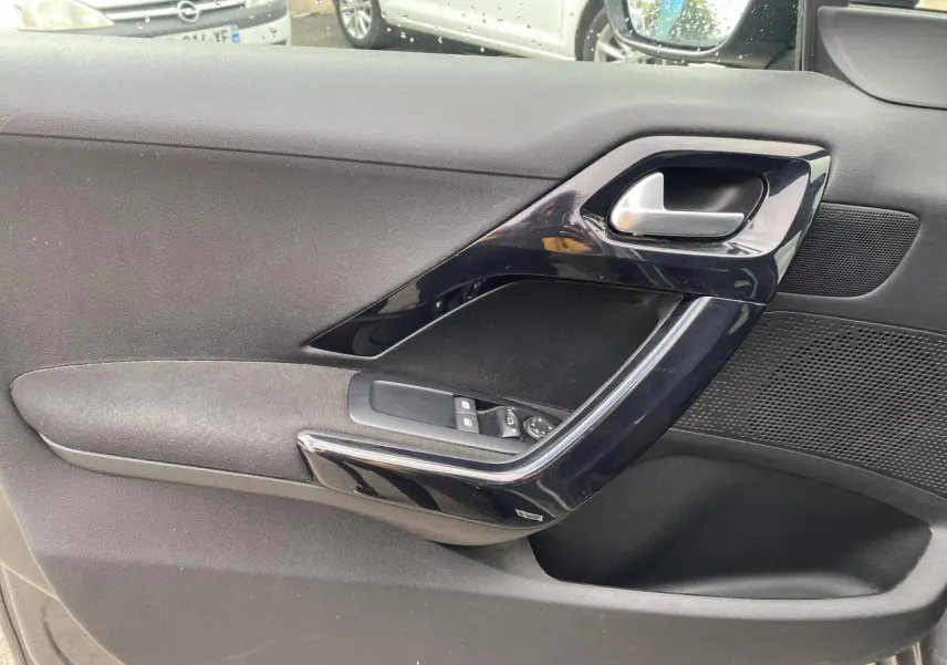 Gros plan sur la contre-porte avant gauche noire avec commandes des vitres électriques et poignée brillante.