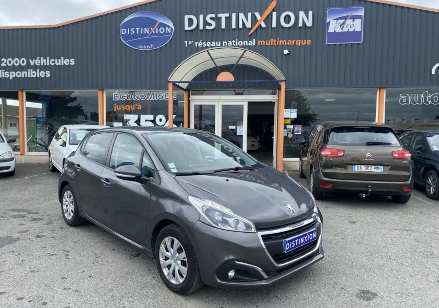 Peugeot 208 gris métallisé vue 3/4 avant droit, stationnée devant un concessionnaire multimarque.