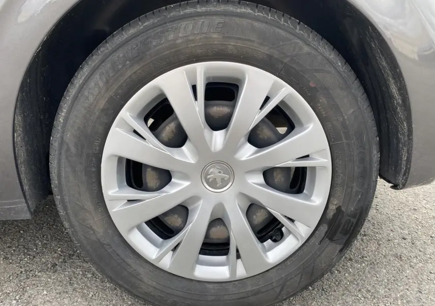 Gros plan sur la roue avant droite d’une Peugeot 208 gris métallisé, avec enjoliveur argenté et logo Peugeot central.