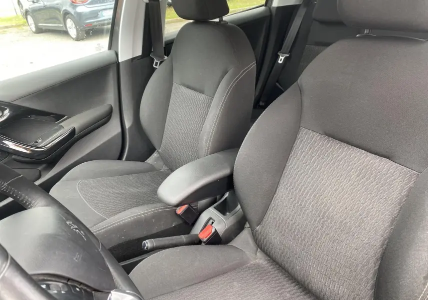 Vue intérieure de la Peugeot 208 gris, montrant les sièges avant avec accoudoir central et partie du volant côté gauche.